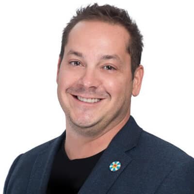 Smiling man with short hair wearing a dark blazer and a black shirt.